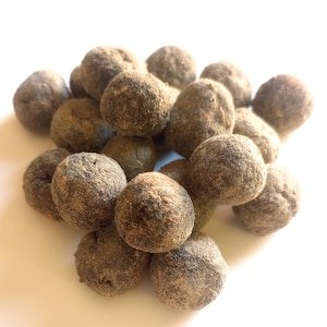 May include: A pile of round, dark brown objects with a textured, slightly rough surface. The objects are clustered together against a bright white background, creating a contrast of light and shadow.