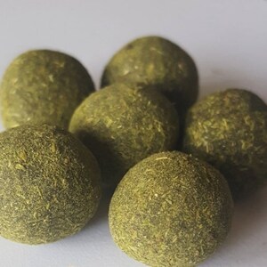 May include: A close-up shot displays six round, green spheres. Each sphere is covered in a textured, dried, leafy material. The spheres are arranged in a loose cluster, with some overlapping. The lighting is soft, highlighting the texture and color of the spheres.