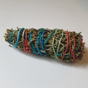 May include: A bundle of dried green leaves, tightly wrapped with colorful twine. The twine is in shades of blue, red, and green, creating a decorative pattern around the bundle. The leaves have a natural, textured appearance.