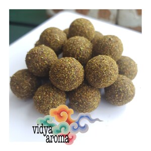 May include: A close-up of a white plate with a pile of round, dark brown balls covered in green herbs. The balls are arranged in a cluster. The image includes the text "vidya aroma" in a stylized font with a colorful design.