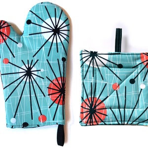 Puede incluir: Un juego de dos manoplas de horno azul turquesa con un patrón geométrico blanco y negro y círculos rojos. La manopla de horno es un posavasos con un lazo para colgar.