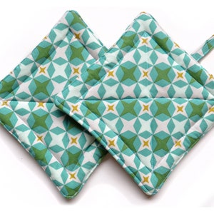 Puede incluir: Un par de agarraderas de olla acolchadas de color verde azulado y verde con un patrón geométrico y detalles dorados.