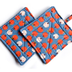 Puede incluir: Un par de agarraderas de olla acolchadas azules con un patrón de manzanas rojas.