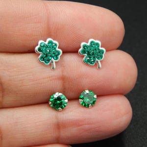 May include: A pair of earrings featuring a four-leaf clover design with green rhinestones and a round green rhinestone earring.