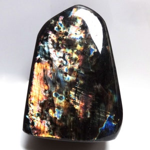May include: A black labradorite gemstone with iridescent blue, green, and gold flashes. The gemstone is polished and has a smooth, rounded shape.