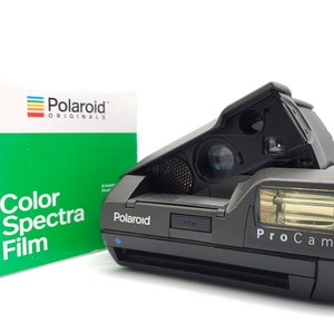 Könnte beinhalten: Eine schwarze Polaroid ProCam Sofortbildkamera mit Blitz und eine Packung Color Spectra Film. Die Filmverpackung ist grün und weiß mit dem Polaroid Originals Logo. Auf der Kamera steht das Wort "Polaroid".