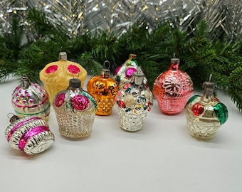 May include: A collection of eight vintage glass Christmas ornaments. The ornaments are shaped like baskets and feature various colors and designs, including pink, green, yellow, and silver.