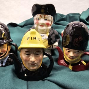 May include: Four ceramic teapots shaped like people in different professions. A policeman, a fireman, a soldier, and a man wearing a top hat. The teapots are all hand-painted and have detailed features.