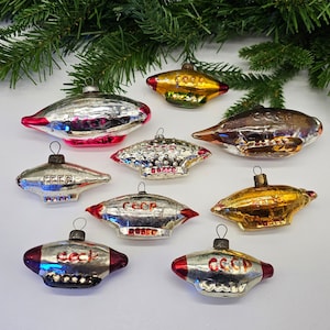 May include: Nine vintage glass ornaments shaped like airships. Each ornament is silver with red accents and features the inscription "CCCP" in Cyrillic lettering. The ornaments are a mix of silver, gold, and red.