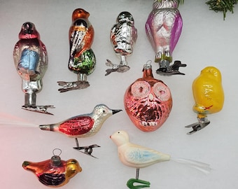 Op de afbeelding: Een verzameling van negen vintage glazen kerstversieringen met verschillende vogel- en uilmotieven. De ornamenten zijn geschilderd in verschillende kleuren, waaronder rood, blauw, groen, geel en wit. Elk ornament heeft een zilveren clip om aan een kerstboom te hangen.
