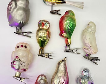 May include: A collection of nine vintage glass ornaments shaped like birds and owls. The ornaments are silver, gold, green, red, white, and blue. They are all hanging from silver clips.