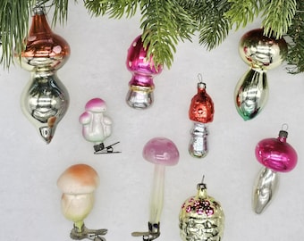 May include: Nine vintage glass Christmas ornaments shaped like mushrooms. The ornaments are in various colors, including pink, red, and white. Some of the ornaments have silver accents. The ornaments are hanging from a Christmas tree.