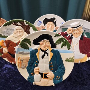 May include: Set of five ceramic plates featuring colourful illustrations of men in various costumes. Each plate has a white background with a blue border.