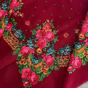 May include: A deep burgundy square scarf featuring a vibrant floral pattern with large pink roses, small blue flowers, and green leaves. The design includes an orange decorative border and small green dots scattered across the solid red background.
