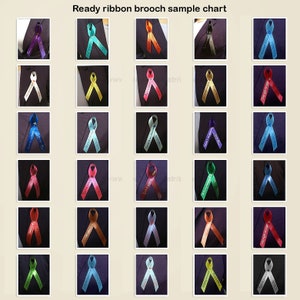 May include: A sample chart of ready ribbon brooches. The brooches are in various colors, including purple, teal, orange, and red. Each ribbon has text on it. The brooches are pinned to a dark fabric.