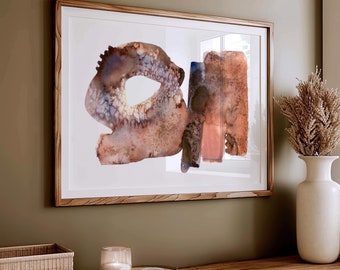 May include: A framed abstract watercolor painting with brown, orange, and blue hues. The painting is hanging on a wall above a wooden shelf with a wicker basket, a candle, and a small plate.