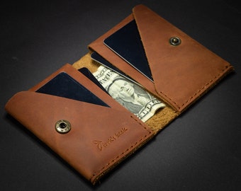 May include: A brown leather wallet with a flap closure and two card slots. The wallet is open and has a dollar bill and two cards inside. The wallet has the text "World's Best" embossed on the front.