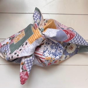 May include: A patchwork fabric wrap, knotted to secure its contents. The fabric displays floral, gingham, and striped patterns in pink, blue, green, and yellow. It's likely used for gift wrapping or storage.