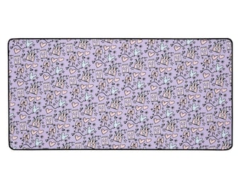 May include: A rectangular lavender desk mat featuring a repeating pattern of castles, bows, hearts, stars, and Mickey Mouse silhouettes in black, pink, and blue. The mat has a black border.