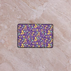 Peut inclure: Un tapis de souris rectangulaire violet avec une bordure noire. Le tapis de souris présente un motif répété de lanternes jaunes, d'étoiles et de caméléons verts. Le motif est sur un fond violet.