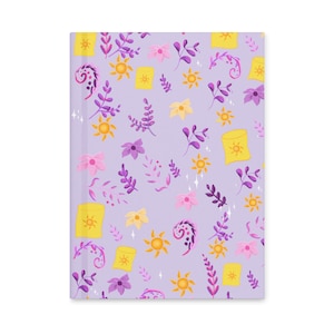Peut inclure: Un carnet lilas avec un motif répété de lanternes jaunes, de soleils et d'éléments floraux violets et roses. Le design est fantaisiste et coloré, avec un thème de conte de fées.