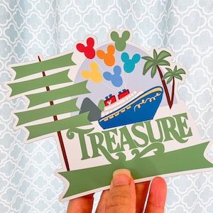 May include: A green and blue sign with a ship, palm trees, and Mickey Mouse heads. The sign says "Treasure" in a whimsical font.