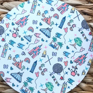 Può includere: Sottobicchiere rotondo bianco con un motivo colorato di varie icone dei parchi Disney, tra cui il castello, Spaceship Earth, tazze da tè e fuochi d'artificio. Lo sfondo è bianco con accenti rosa, blu e verdi.