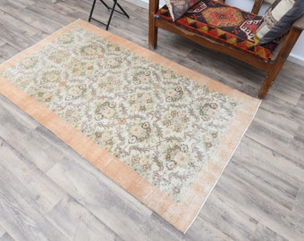 May include: A vintage rug with a floral pattern in shades of beige, cream, and brown. The rug has a peach-colored border.