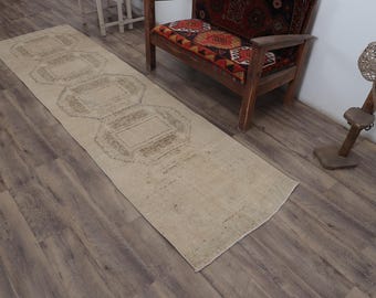 Op de afbeelding: Een beige loper met een geometrisch patroon in een donkerdere beige kleur. De loper ligt op een houten vloer.