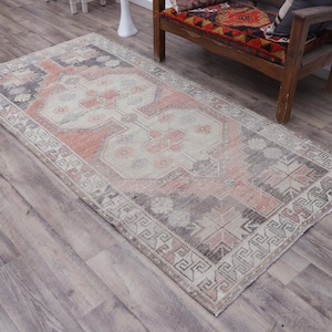 Puede incluir: Una alfombra de estilo vintage con un esquema de color rosa y gris descolorido. La alfombra tiene un patr&oacute;n geom&eacute;trico con un medall&oacute;n central y un borde de motivos repetidos.