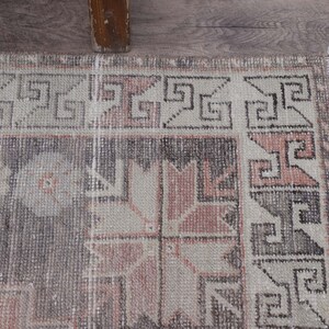 Puede incluir: Una alfombra vintage con un patr&oacute;n geom&eacute;trico en tonos rosa, gris y blanco. La alfombra tiene un borde deshilachado y un aspecto desgastado.
