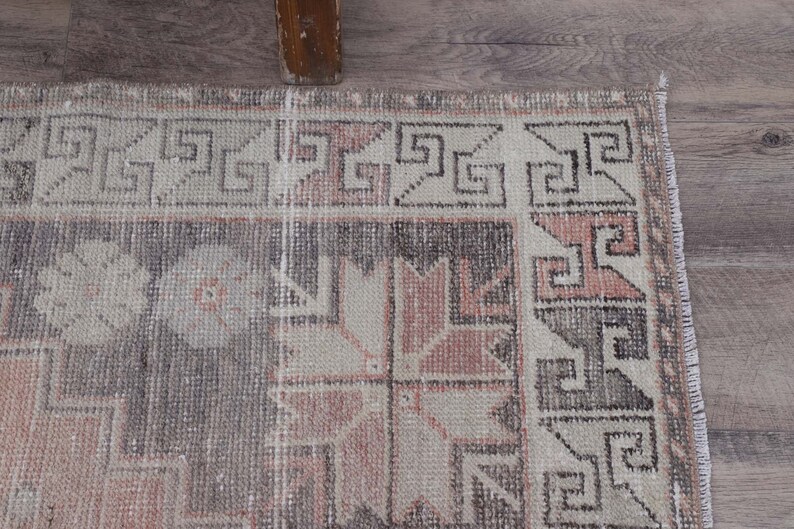 Puede incluir: Una alfombra vintage con un patr&oacute;n geom&eacute;trico en tonos rosa, gris y blanco. La alfombra tiene un borde deshilachado y un aspecto desgastado.