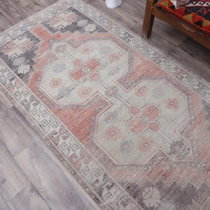 Puede incluir: Una alfombra vintage con un esquema de color rosa y crema descolorido. La alfombra tiene un dise&ntilde;o persa tradicional con intrincados patrones florales y un borde geom&eacute;trico.