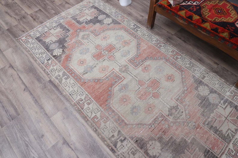 Puede incluir: Una alfombra vintage con un esquema de color rosa y crema descolorido. La alfombra tiene un dise&ntilde;o persa tradicional con intrincados patrones florales y un borde geom&eacute;trico.