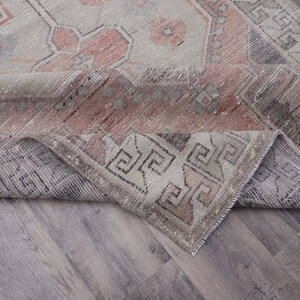 Puede incluir: Una alfombra vintage con un patr&oacute;n geom&eacute;trico rosa y gris descolorido. La alfombra est&aacute; doblada por la mitad, mostrando el rev&eacute;s de la tela.