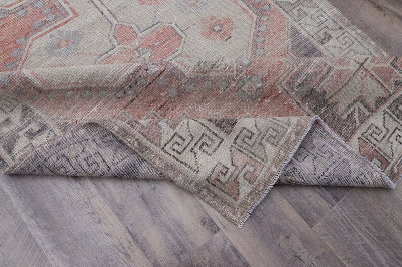 Puede incluir: Una alfombra vintage con un patr&oacute;n geom&eacute;trico rosa y gris descolorido. La alfombra est&aacute; doblada por la mitad, mostrando el rev&eacute;s de la tela.