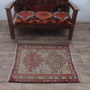 Könnte beinhalten: Ein kleiner, rechteckiger Teppich mit cremefarbenem Hintergrund und einem roten, grünen und blauen geometrischen Muster. Der Teppich hat einen Fransenrand.