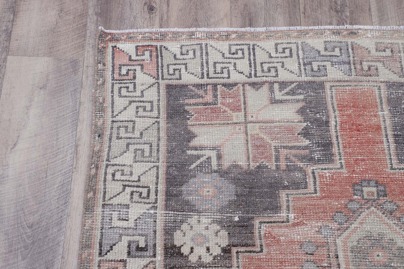 Puede incluir: Una alfombra vintage con un patr&oacute;n geom&eacute;trico en tonos de rosa, gris y blanco. La alfombra tiene un aspecto descolorido y desgastado, lo que le da un aspecto &uacute;nico y antiguo.