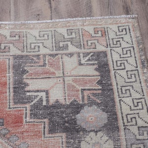 Puede incluir: Una alfombra vintage con un patr&oacute;n geom&eacute;trico en tonos rosa, gris y blanco. La alfombra tiene un borde de flecos.