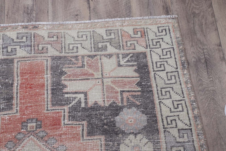 Puede incluir: Una alfombra vintage con un patr&oacute;n geom&eacute;trico en tonos rosa, gris y blanco. La alfombra tiene un borde de flecos.