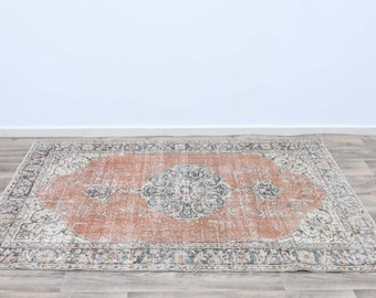 May include: A vintage-style rug with a faded peach-colored center and a white and gray patterned border. The rug has a distressed look and a worn appearance.