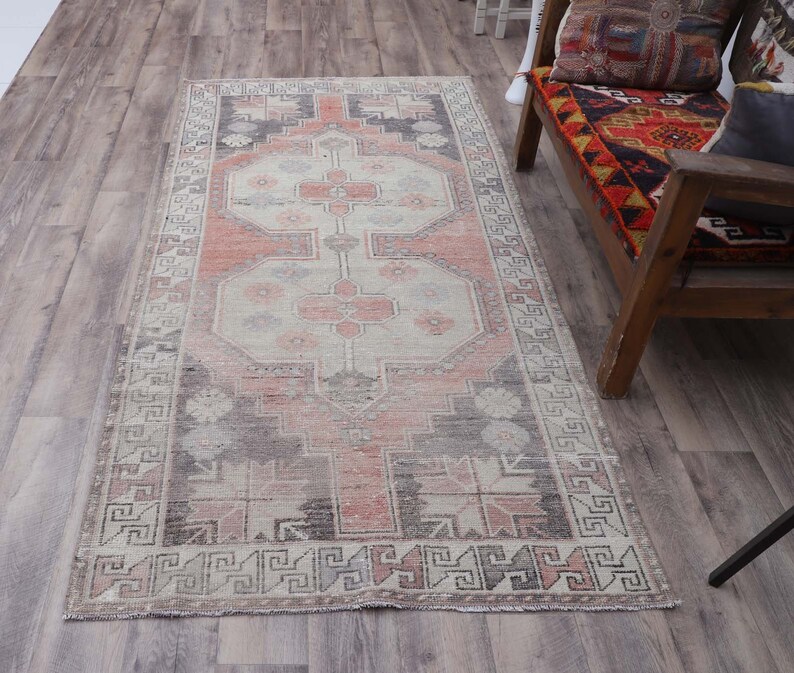 Puede incluir: Una alfombra turca vintage con un patr&oacute;n geom&eacute;trico tradicional en tonos de rosa, gris y blanco. La alfombra tiene un aspecto descolorido y desgastado, perfecto para agregar un toque de estilo bohemio a cualquier habitaci&oacute;n.