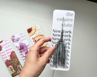 May include: A set of rectangular bookmarks featuring state-themed designs. One bookmark displays the Empire State Building with "New York" repeated. Other bookmarks show a flower, a peach, and a floral scene with text.