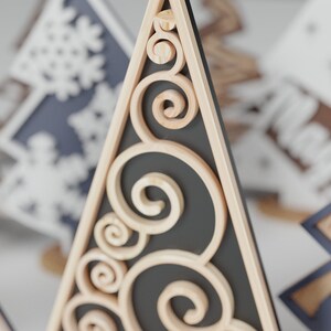 May include: A wooden Christmas tree ornament with a black background and intricate scrollwork details.