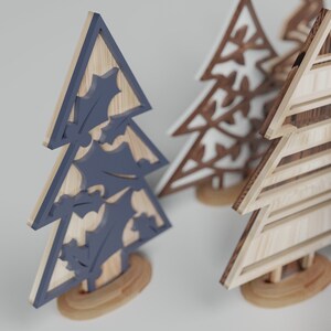 May include: Three wooden Christmas tree ornaments. One is painted blue with holly leaves, one is white with a snowflake design, and one is natural wood with a striped pattern.