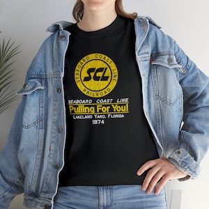 Lifestyle: woman in Black Seaboard Coast Line Railroad shirt with denim jacket, facing left