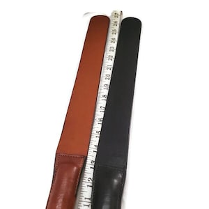 May include: Two leather strops, one brown and one black, are displayed side-by-side against a white background. A measuring tape is placed between them, showing the length of the strops. The brown strop is approximately 26 inches long.