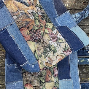 May include: A patchwork tote bag made from denim and tapestry fabric. The tapestry features a rabbit, flowers, and fruit. The bag has denim handles and is constructed with various shades of blue denim.