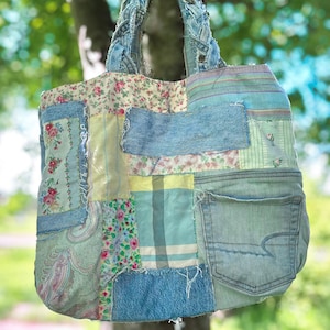 May include: A patchwork tote bag constructed from various fabric scraps including blue denim, floral prints, and plaid patterns. The bag features a braided denim handle and an external denim pocket on the right side with frayed edges.