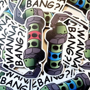 May include: Sticker sheet featuring cartoon-style grenade designs. The grenades are green with black accents and feature red and blue bands. Text on the stickers reads "WANNA BANG?!" in black, bold font.